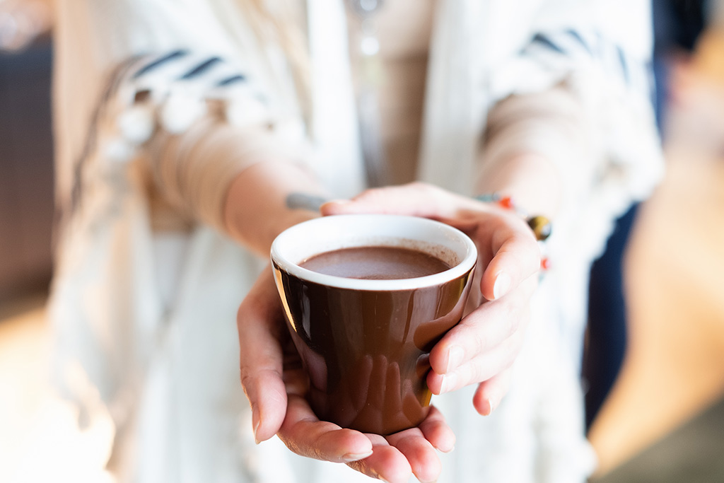 Een vrouw biedt een kop warme chocolademelk aan.