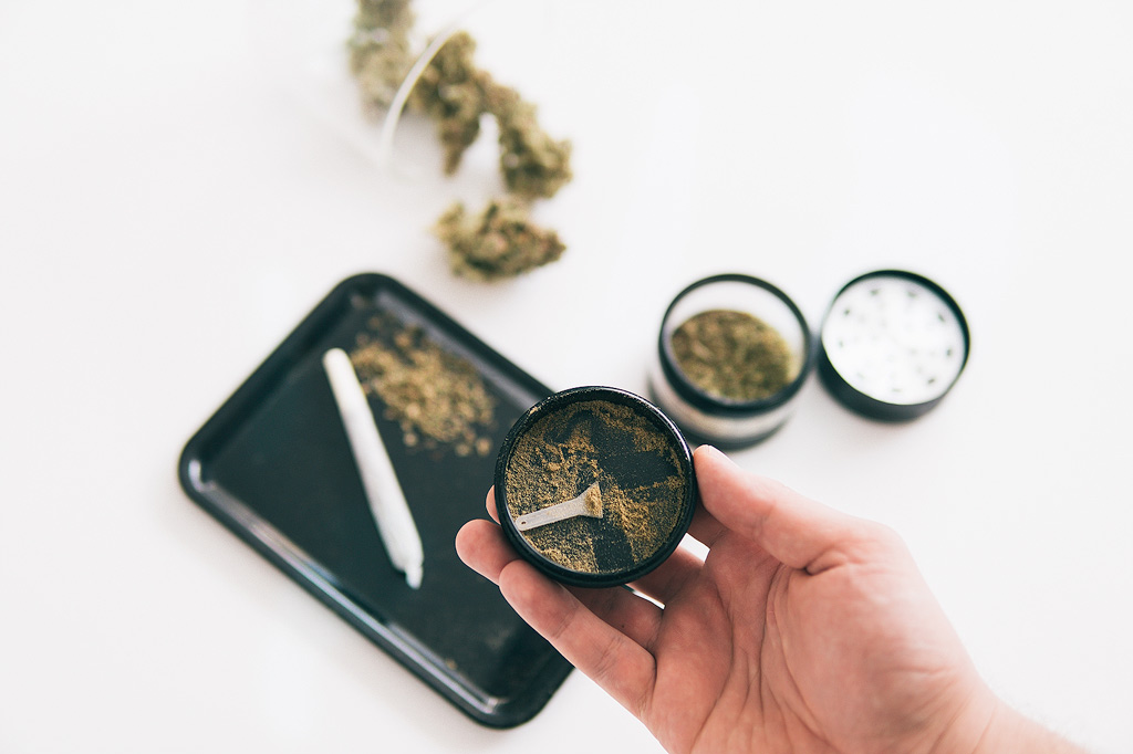 Kief in een grinder met een rolling tray en joint op de achtergrond.